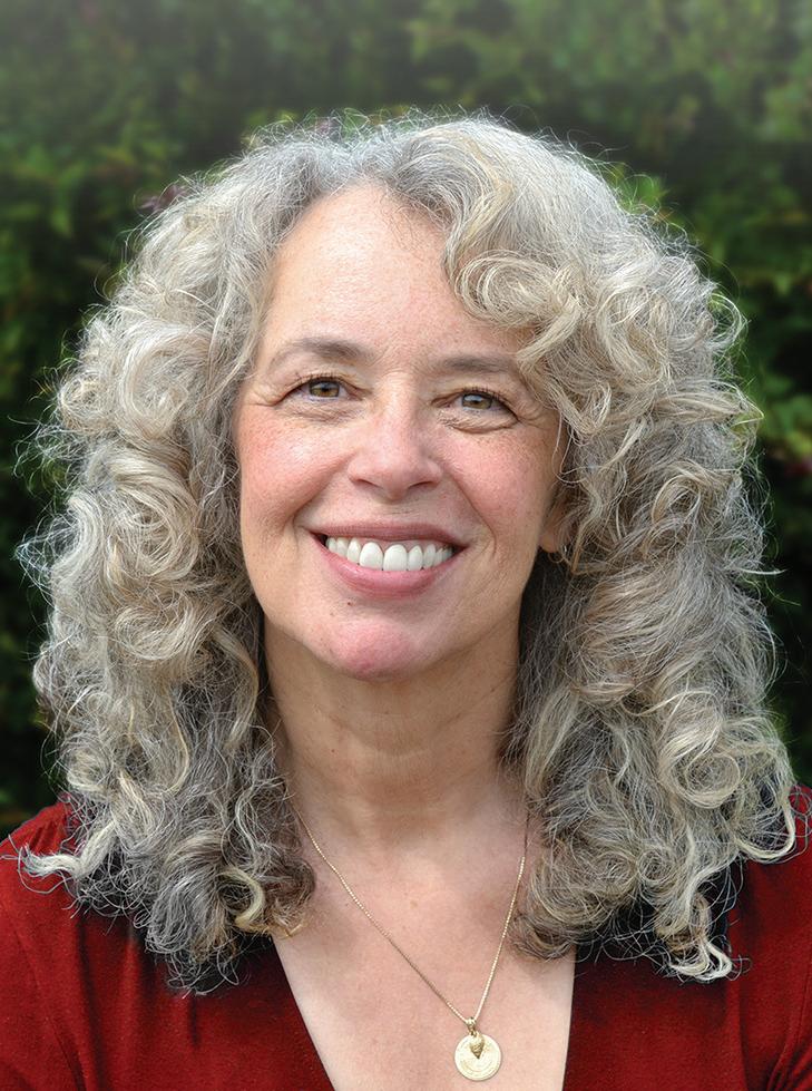 Woman with gray curly hair wearing a red shirt and pendant necklace smiles at the camera against a green background.