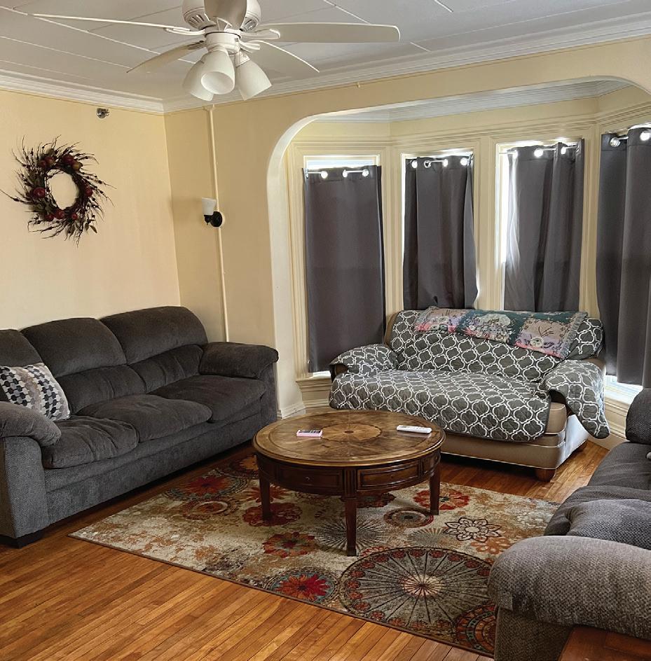 Bright yellow living room with dark sofas, wooden coffee table, patterned rug, and wreath decoration on wall.